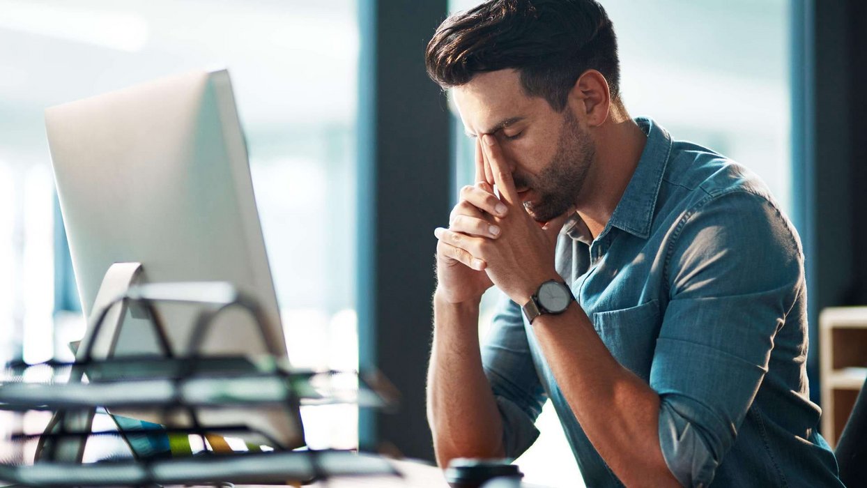 Mitarbeiter sitzt vor Bildschirm und legt nachdenklich Kopf auf die Hände Mitarbeiter sitzt vor Bildschirm und legt nachdenklich Kopf auf die Hände