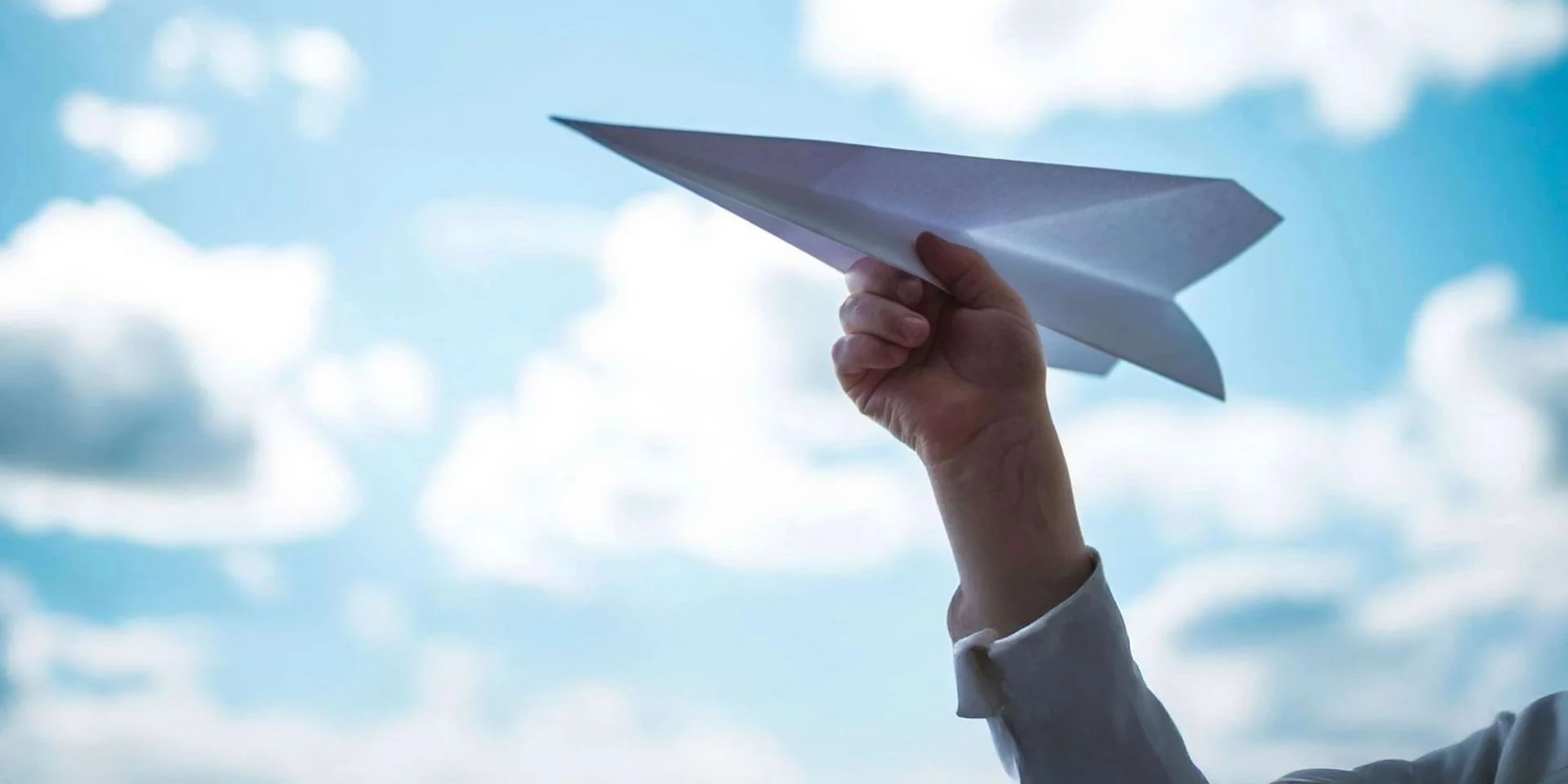 Hand hält Papierflieger in den Himmel