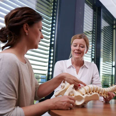 Fachärztin Orthopädie erklärt Patientin Wirbelsäulenmodell